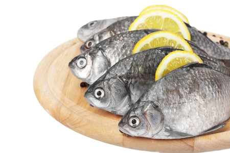 Fresh fishes with lemon and spice on wooden cutting board isolated on white 