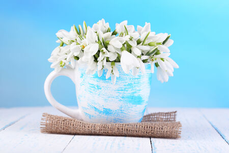 Beautiful snowdrops in vase, on wooden table on bright backgroundの写真素材