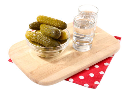 Glasses of vodka and salted cucumbers on wooden board isolated on whiteの写真素材