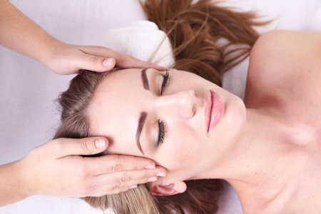 Beautiful young woman having head massage in spa salonの写真素材