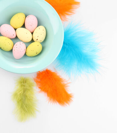 Easter eggs in bowl and decorative feathers isolated on whiteの写真素材