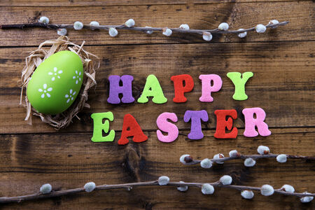 Easter egg in nest, pussy-willow and sign on color wooden background