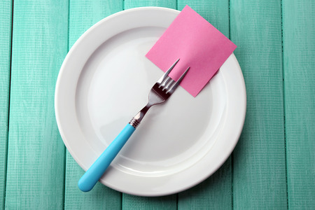Empty note paper attached to fork, on plate, on color wooden background の写真素材