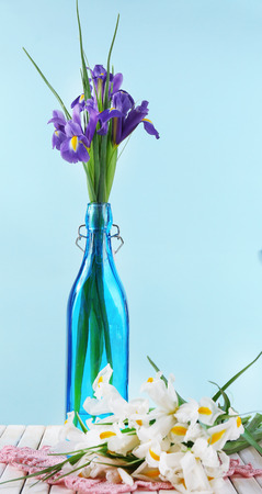 Beautiful irises and daffodils in bottle, on blue backgroundの写真素材