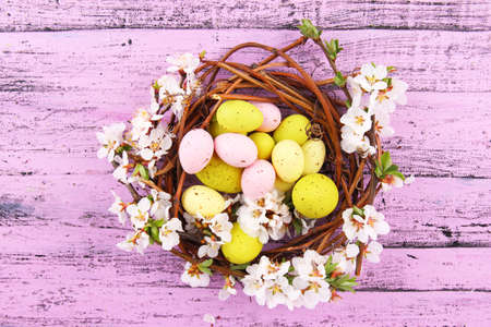 Composition with Easter eggs and blooming branches in nest, on wooden background
