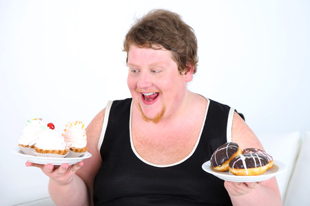Fat man  holding plates with bad unhealthy food on home interior backgroundの写真素材