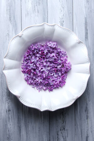Beautiful lilac flowers on white plate on color wooden backgroundの写真素材