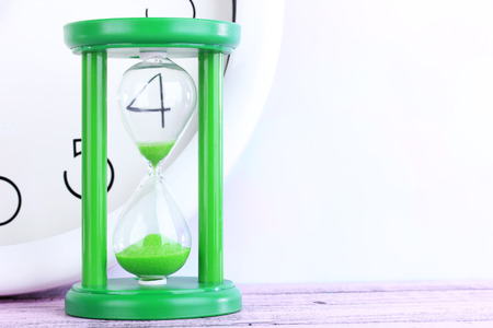 Hourglass and big clock on light background
