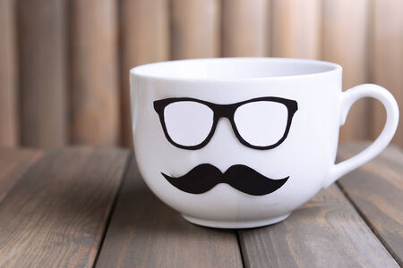 Cup with mustache on table on wooden backgroundの写真素材