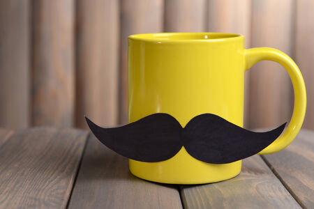 Cup with mustache on table on wooden backgroundの写真素材