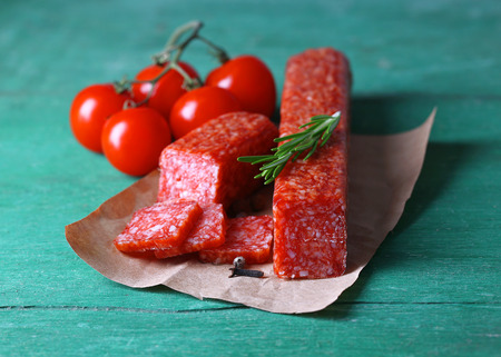Tasty salami sausage, vegetables and spices on paper wooden backgroundの写真素材