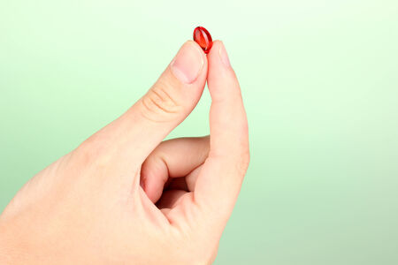 Woman's hand holding a red pill on green background close-upの写真素材