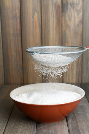 Sifting flour into bowl on table on wooden backgroundの写真素材