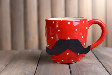 Cup with mustache on table on wooden backgroundの写真素材