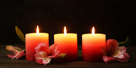 Beautiful candles with flowers on wooden table, on dark backgroundの写真素材