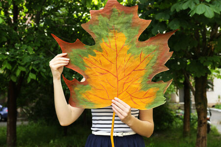 Girl holding decorative maple leaf in parkの写真素材