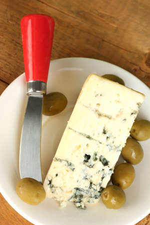 Cheese with mold and olives on the plate and knife on wooden background close-upの写真素材