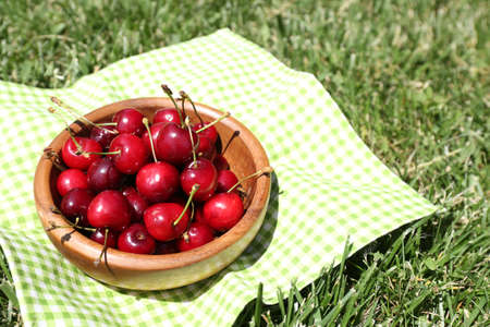 Sweet ripe cherries in wooden bowl, on napkin, on green grass backgroundの写真素材