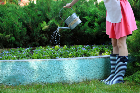 Young woman in rubber boots holding watering can, outdoorsの写真素材