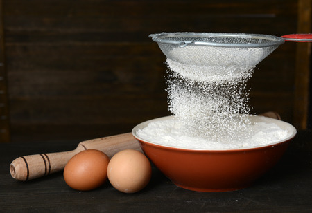 Sifting flour into bowl on table on wooden background