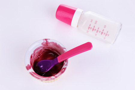 Baby bottle with milk and dirty bowl isolated on whiteの写真素材