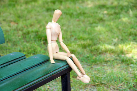 Wooden pose puppet sitting on bench outdoorsの写真素材