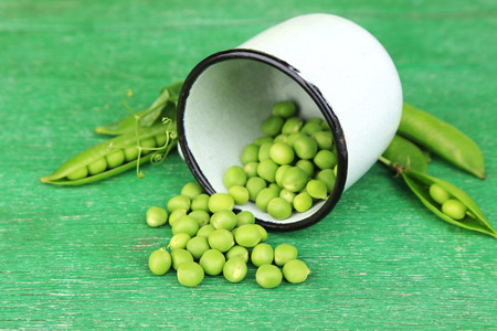 Fresh green peas in metal cup on wooden tableの写真素材