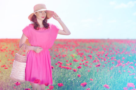 Beautiful young woman holding wicker bag in poppy fieldの写真素材