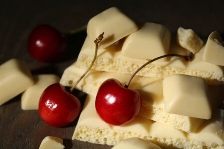 White broken chocolate bar and fresh cherries, on color wooden background