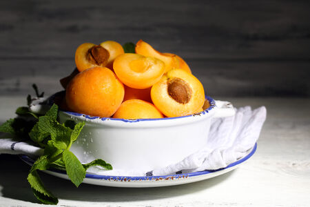 Ripe apricots with green mint leaves in bowl on color wooden backgroundの写真素材