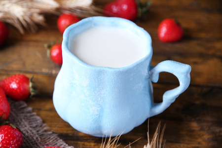 Ripe sweet strawberries and mug with milk on color wooden backgroundの写真素材
