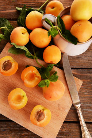 Ripe apricots with green mint leaves on cutting board, on wooden backgroundの写真素材