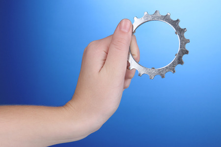 Man holding metallic cogwheel in his hand on blue backgroundの写真素材