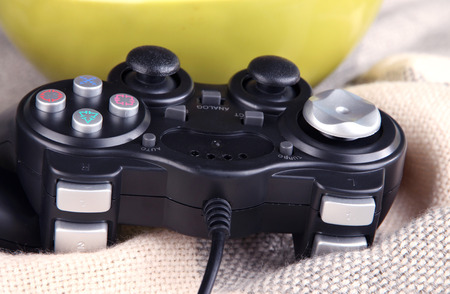 Black game controller and bowl with pop corn on color plaid background