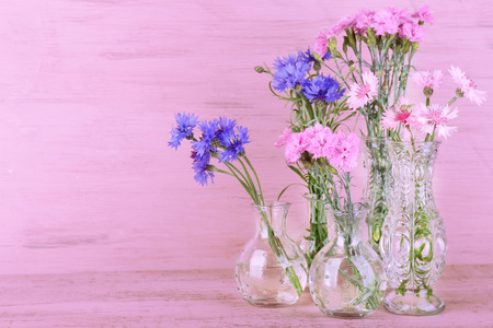 Beautiful summer flowers in vases on pink wooden backgroundの写真素材