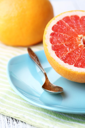 Half of grapefruit, glass jug with fresh juice and spoon on plate on light backgroundの写真素材