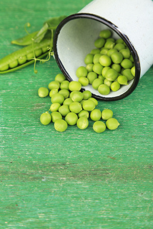 Fresh green peas in metal cup on wooden tableの写真素材