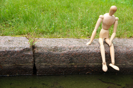 Wooden pose puppet sitting on stone, outdoorsの写真素材