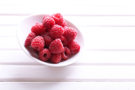 Ripe sweet raspberries in bowl on table close-up