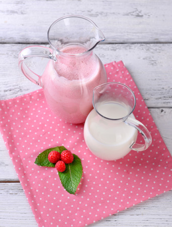 Glass jug of milk cocktail with raspberry taste on wooden table, on light backgroundの写真素材