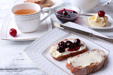 Fresh bread with cherry jam and homemade butter on plate on wooden backgroundの写真素材
