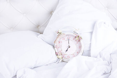 Metal clock on pillows on a big white bedの写真素材