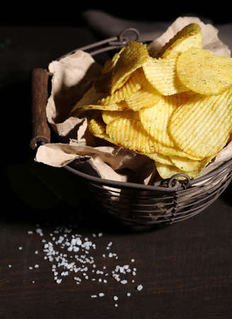 Tasty potato chips in metal basket  on wooden table with dark lightの写真素材