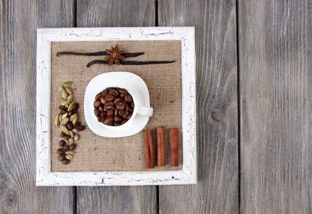 Wooden frame with white mug, coffee grains and spices on wooden backgroundの写真素材