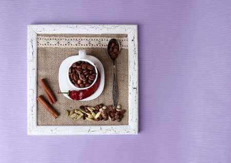 Wooden frame with white mug, coffee grains and spices on color backgroundの写真素材