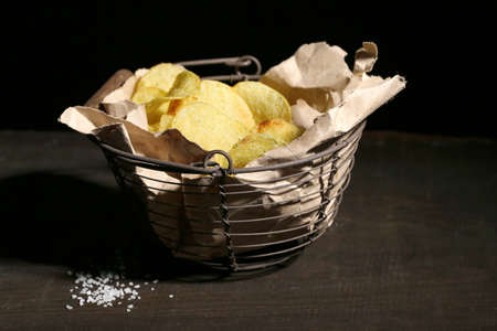Tasty potato chips in metal basket  on wooden table with dark light