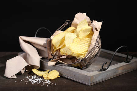 Tasty potato chips in metal basket  on wooden table with dark lightの写真素材