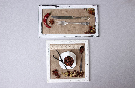 Wooden frames with white mug, cutlery, coffee grains and spices on wooden background