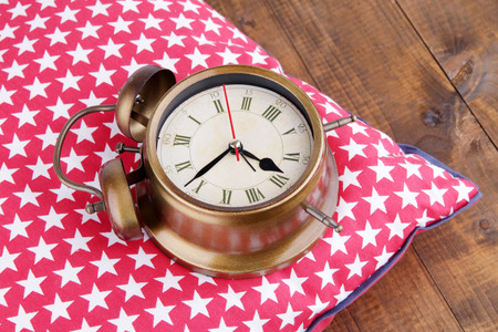 Metal clock on a red pillow with white stars on wooden background