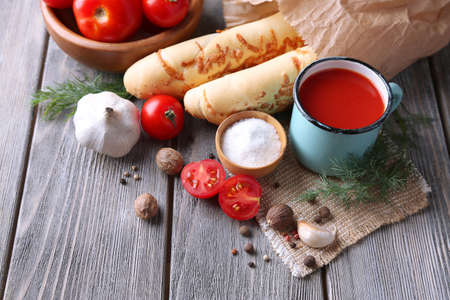 Homemade tomato juice in color mug, bread sticks, spices and fresh tomatoes on wooden backgroundの写真素材